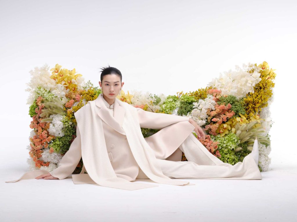 chinese model in light beige coat outfit in front of a cat head shaped real flower wall