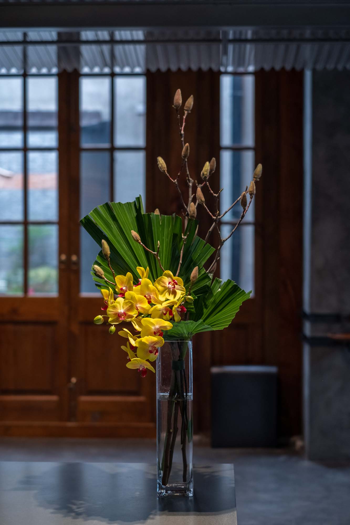 flower arrangement in vase with phalaenopsis orchid, palm leaves and magnolia branches by Florist and set designer in Shanghai China Daria Bokova